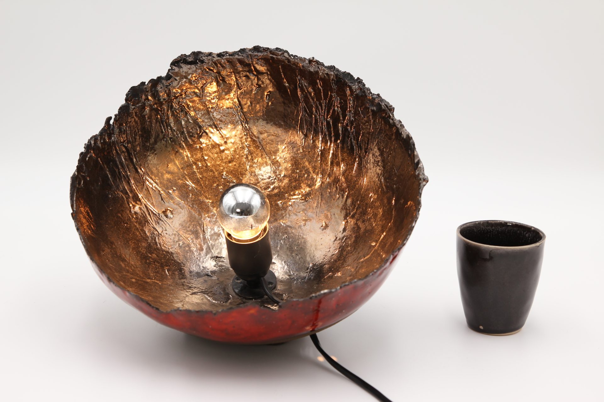lampe en terre chamottée émaillée vue de dessus avec une tasse qui précise la taille de la lampe