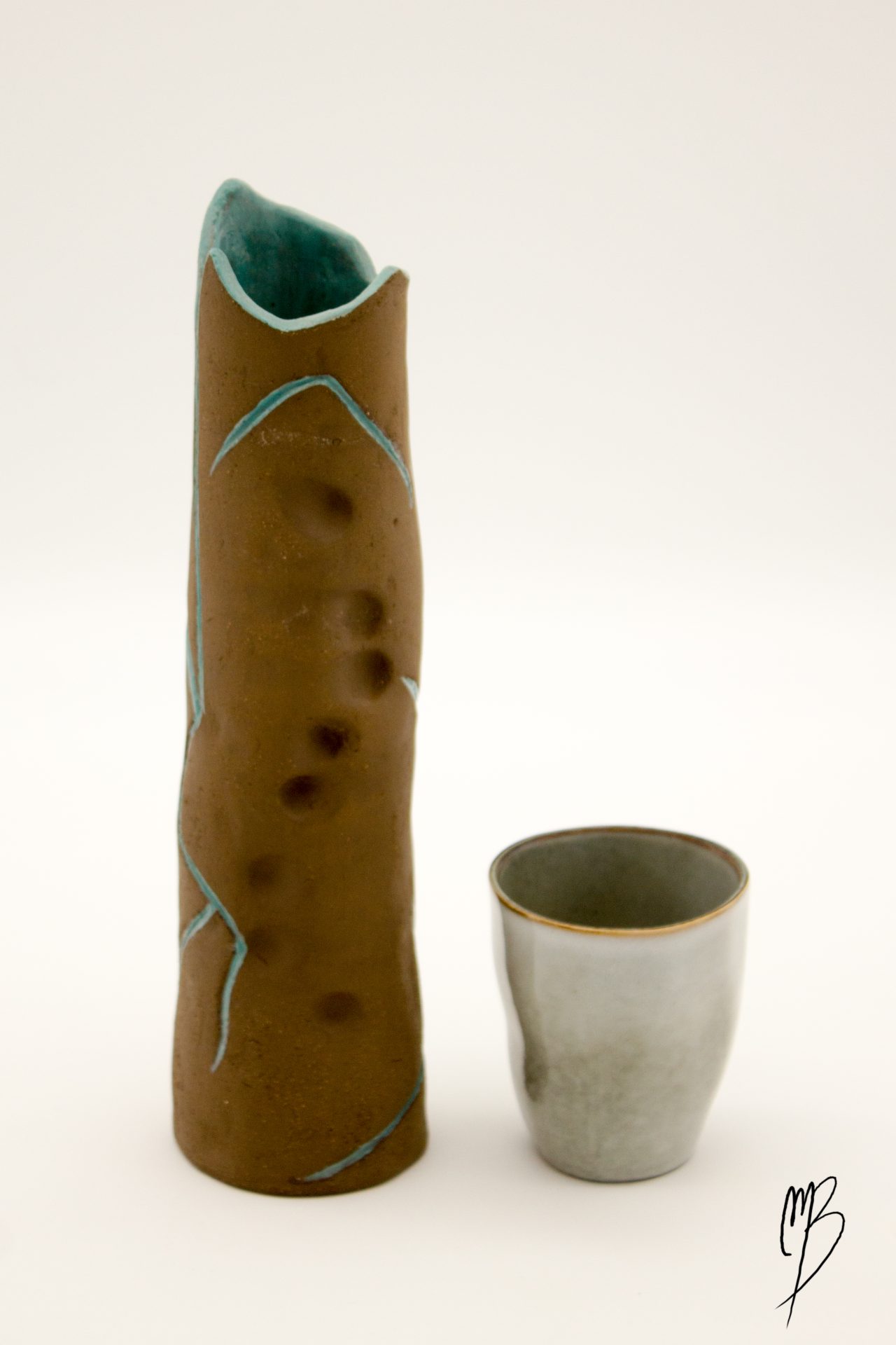 modelages sculptures d'un vase haut et fin orné d'un tronc d'arbre abstrait marron strié de bleu en terre émaillé, accompagné d'une tasse reflétant la taille du vase
