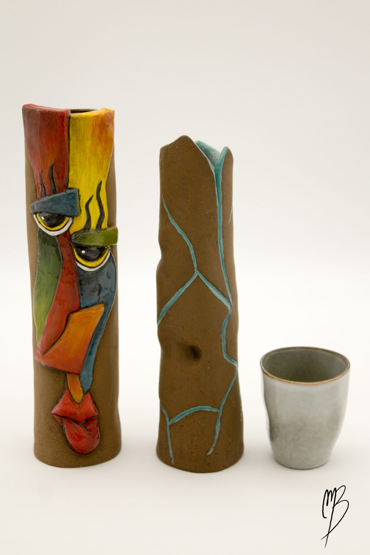 modelages sculptures d'un vase haut et fin orné d'un visage abstrait de couleur rouge jaune vert et bleu et d'un autre vase haut et fin orné d'un tronc d'arbre abstrait, accompagnés d'une tasse reflétant la taille des vases