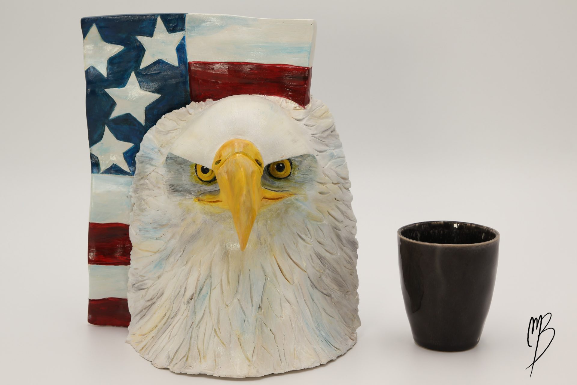 Animaux. Tête d'aigle et drapeau américain en terre cuite recouverts de peinture acrylique vernie. vue comparative à une tasse pour la taille