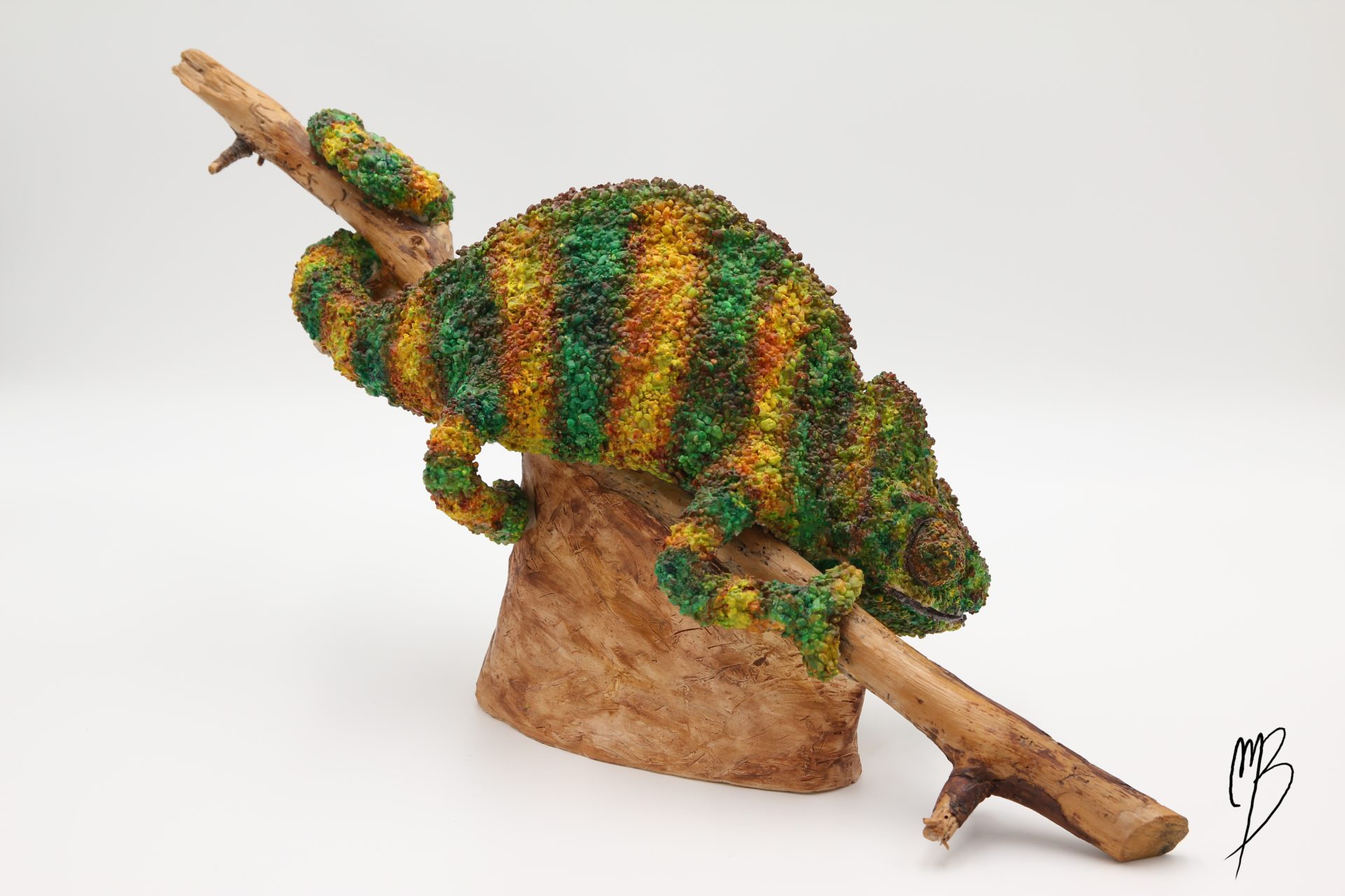 Animaux. Caméléon sur sa branche en terre cuite recouvert de sable et de peinture acrylique vernie. Vue de côté