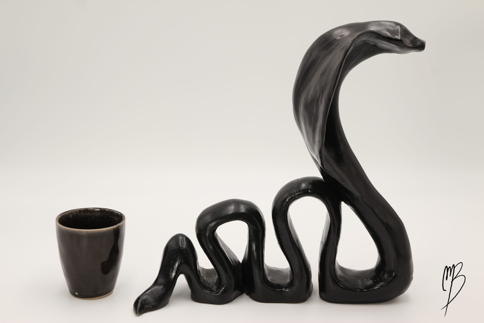 Animaux. Cobra prêt à attaquer en terre cuite recouverts de peinture acrylique noire vernie. Vue comparative à une tasse pour la taille