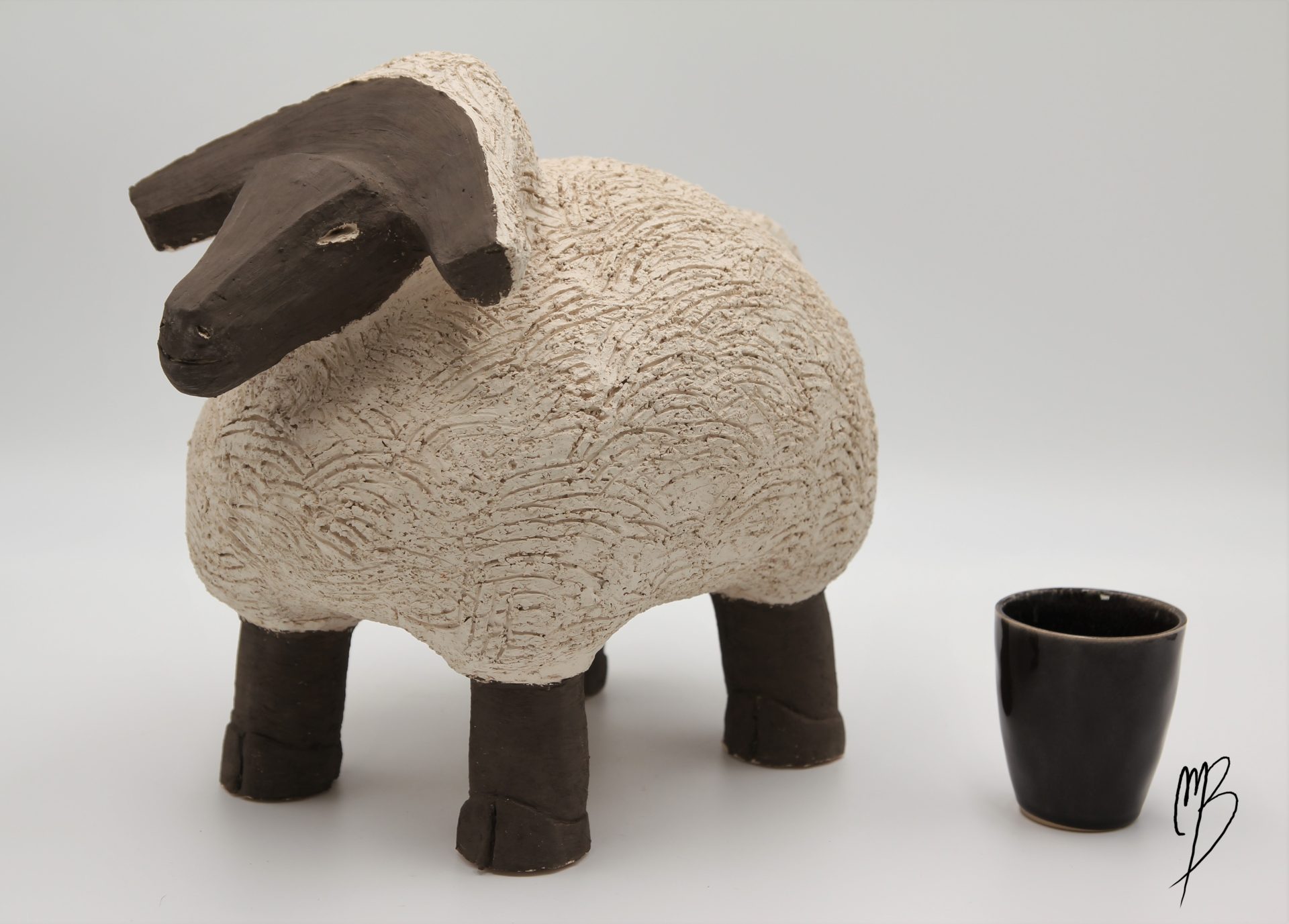 Animaux. Bélier en terre chamottée blanche cuite recouverts d'une barbotine mate. Vue comparative à une tasse pour la taille
