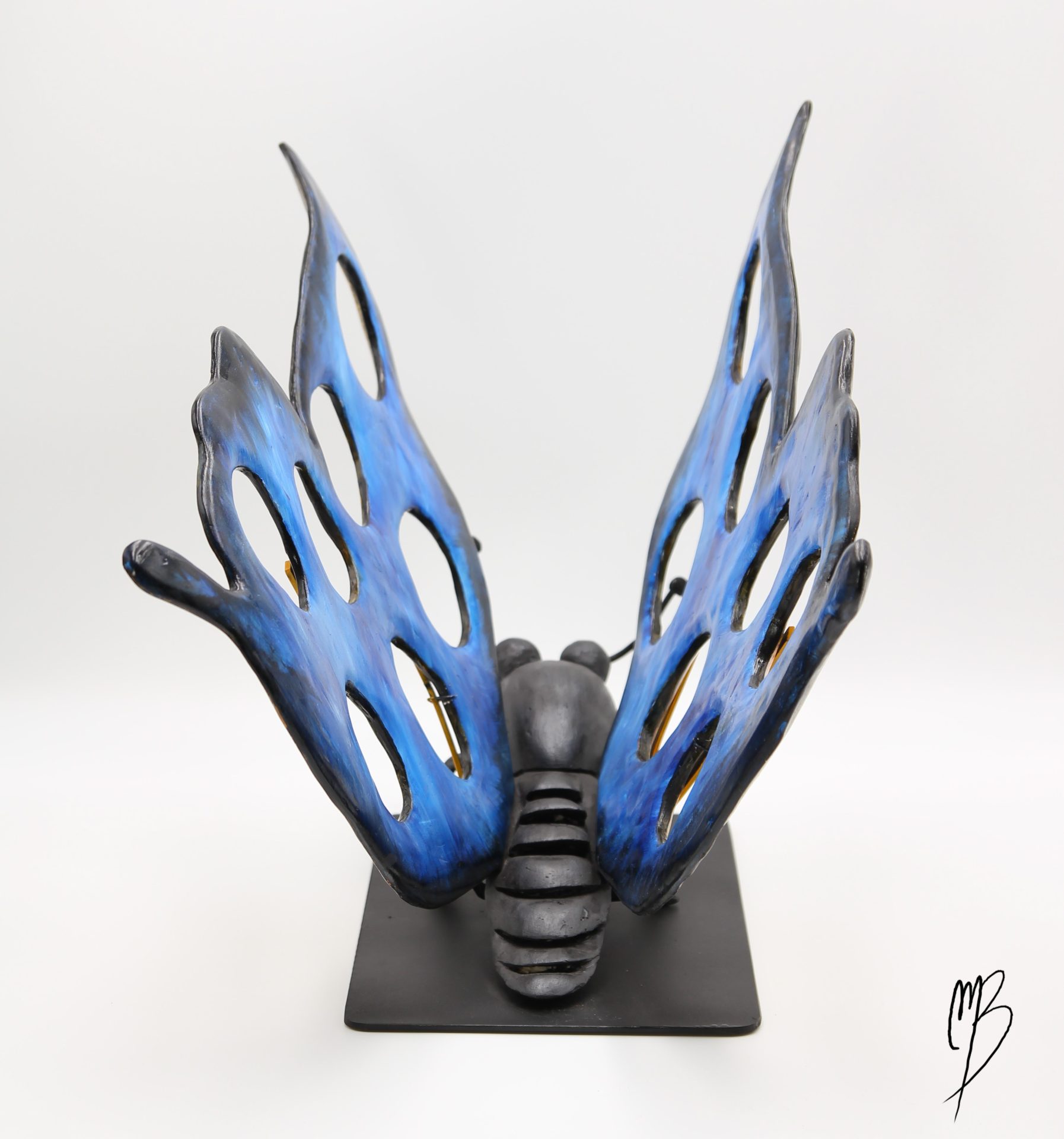 Animaux. Morpho Bleu aux ailes déployées jaunes et bleues sur un socle en métal en terre cuite recouverts de peinture acrylique vernie. Vue de dessus arrière