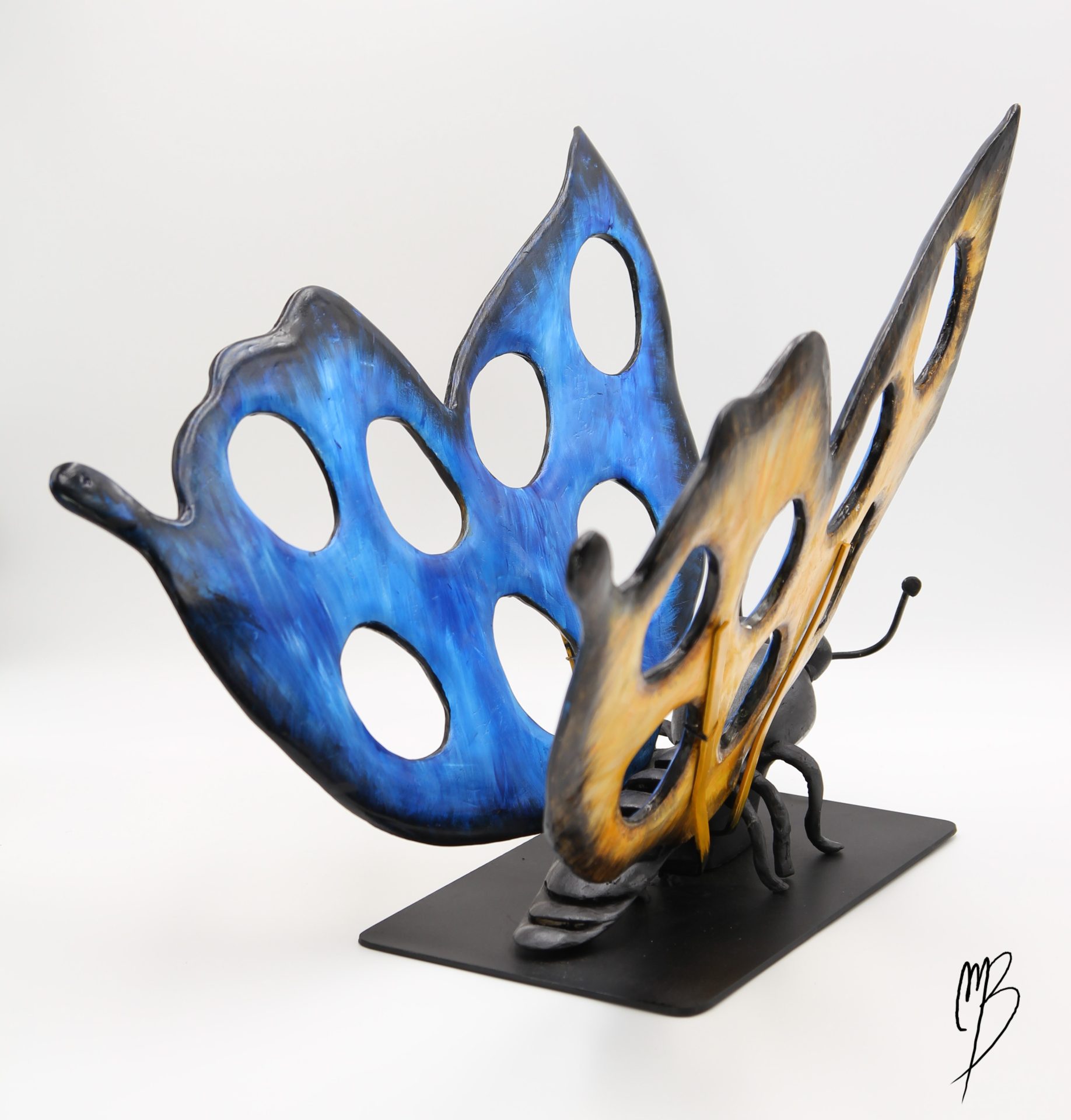 Animaux. Morpho Bleu aux ailes déployées jaunes et bleues sur un socle en métal en terre cuite recouverts de peinture acrylique vernie.