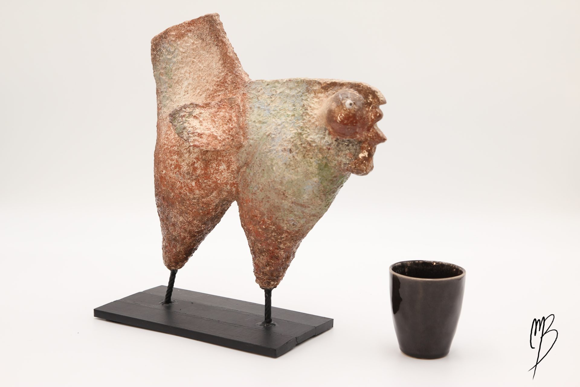 Animaux. Poule stylisée de couleurs mouchetées rouille et blanche sur un socle en métal en terre cuite recouverts de peinture acrylique vernie. Vue comparative à une tasse pour la taille
