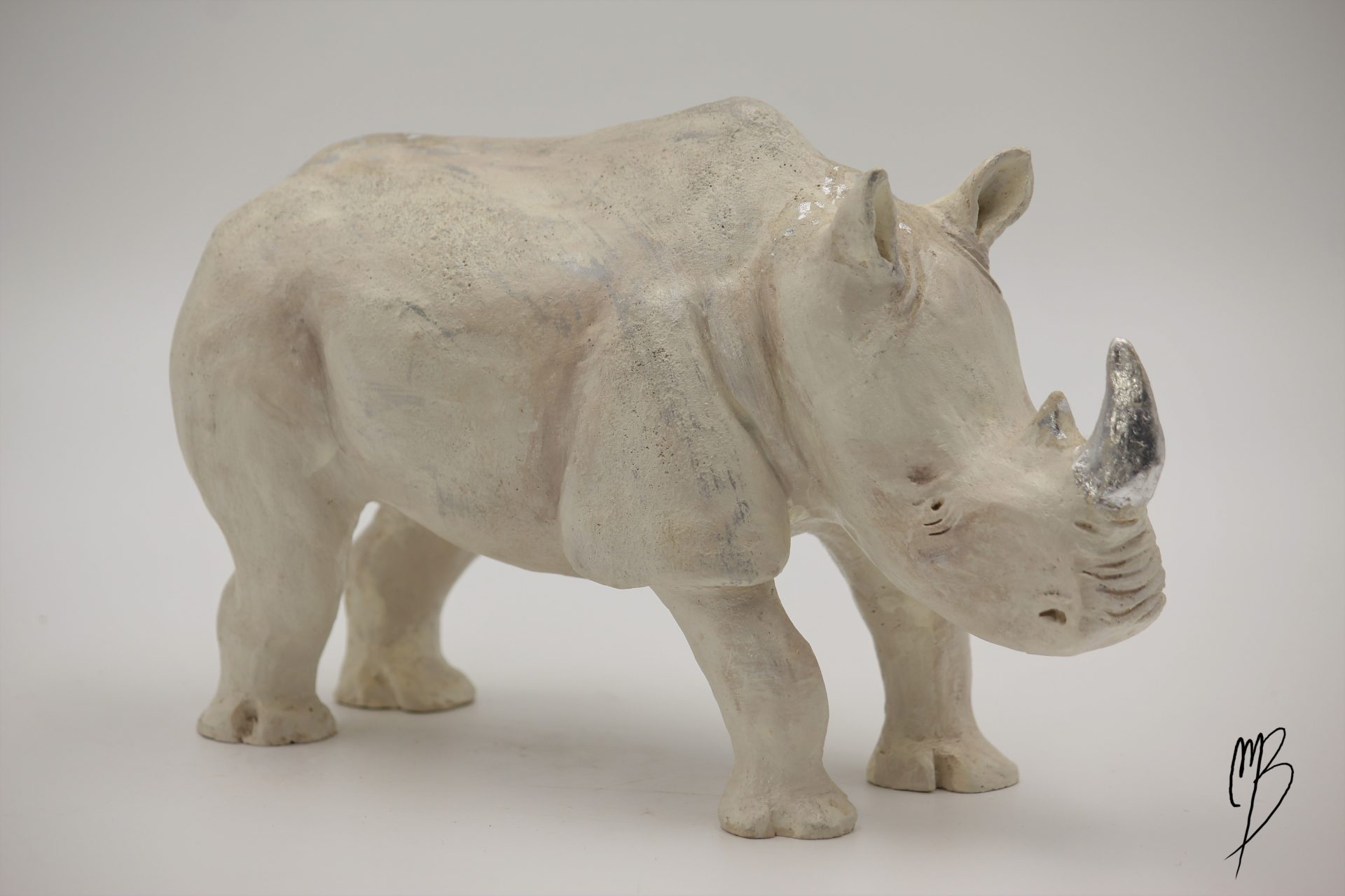Animaux. Rhinocéros en terre cuite recouvert de peinture acrylique et de feuilles d'argent. Vue de côté.