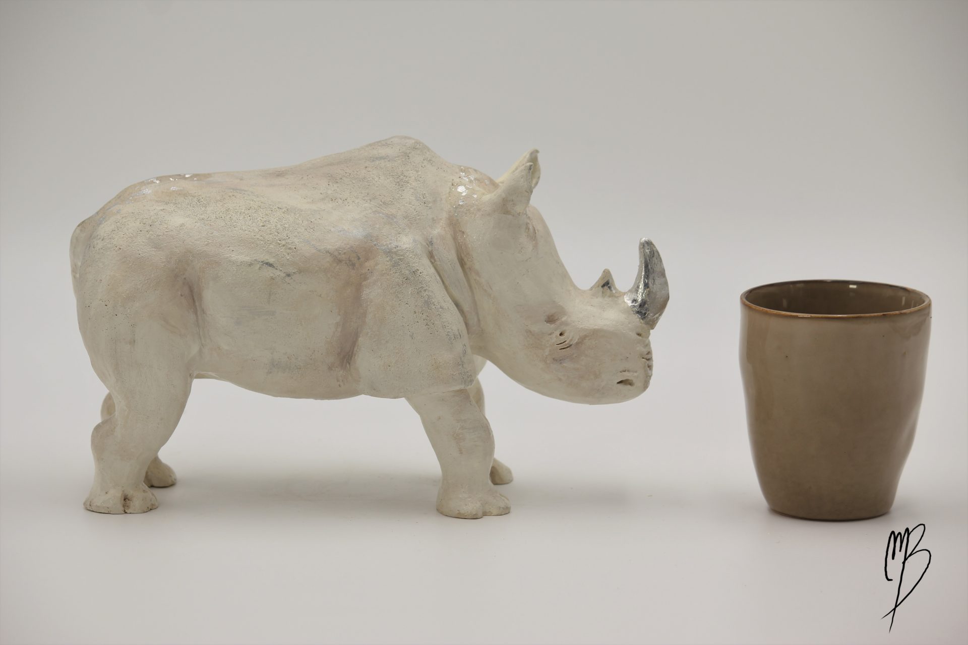 Animaux. Rhinocéros en terre cuite recouvert de peinture acrylique et de feuilles d'argent. Vue comparative à une tasse pour la taille.