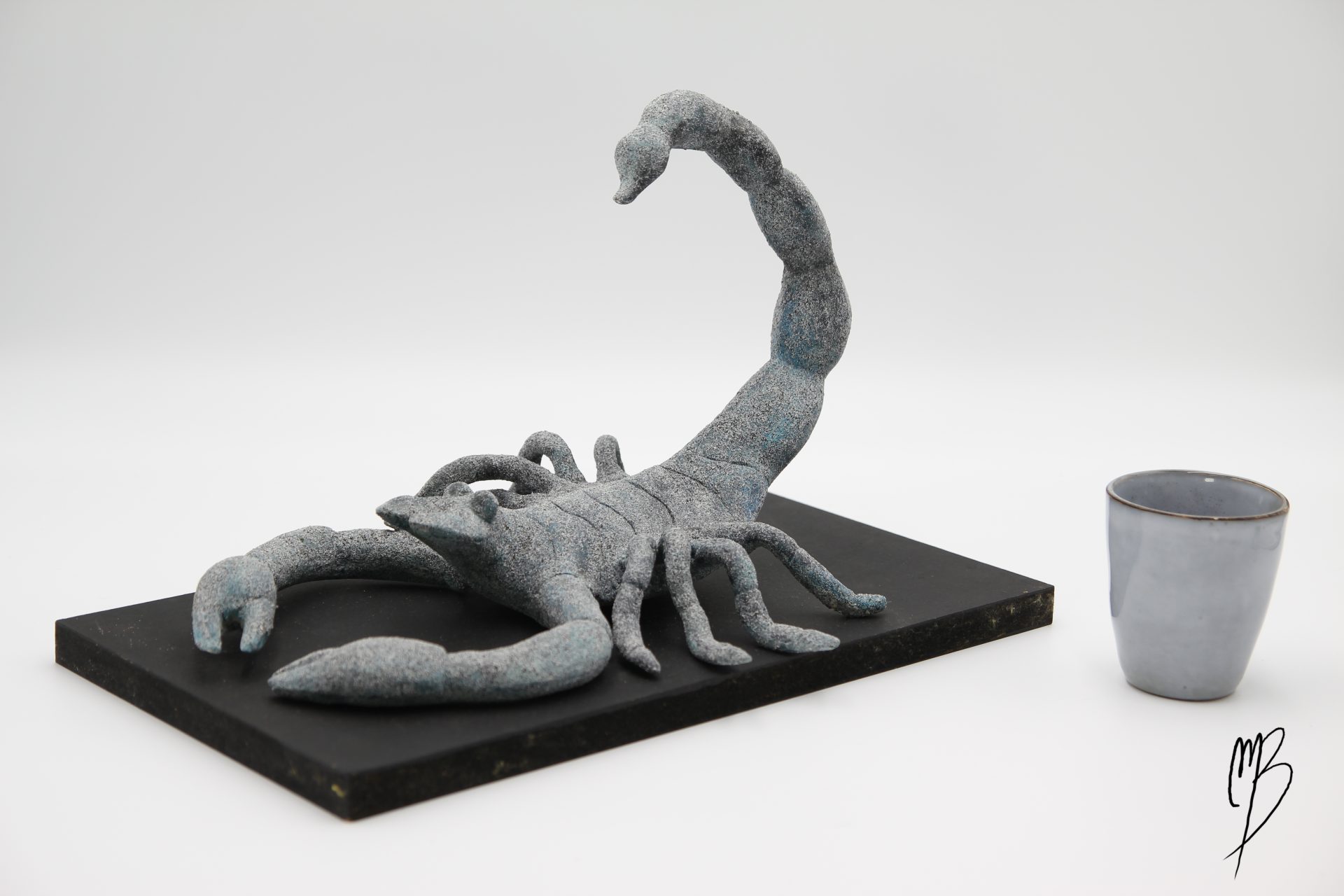 Animaux. Scorpion sur son socle en terre cuite recouvert de peinture acrylique sablée. Vue comparative à une tasse pour la taille