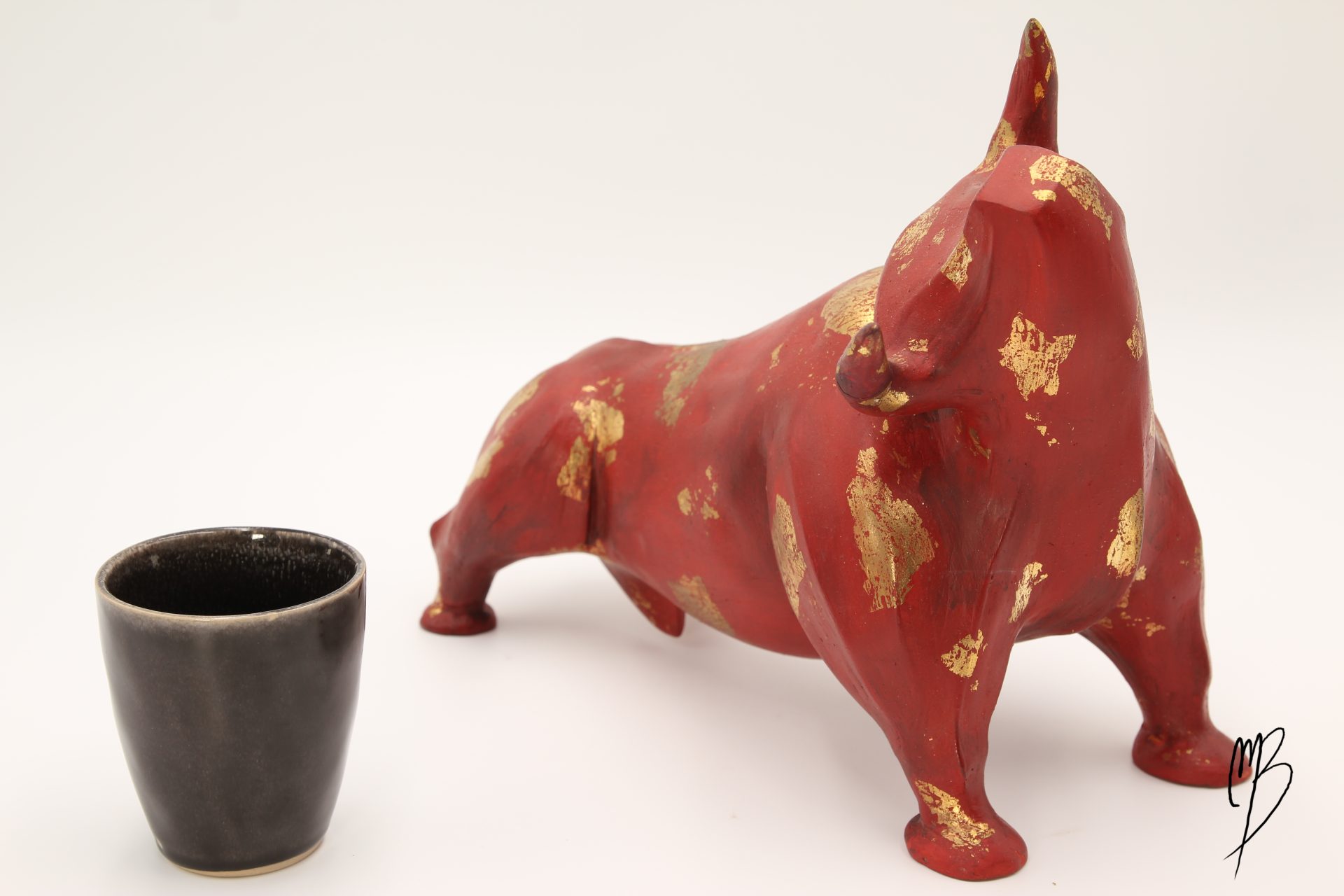 Animaux. Taureau rouge en terre cuite recouvert de peinture acrylique et de feuilles d'or. Vue comparative à une tasse pour la taille.