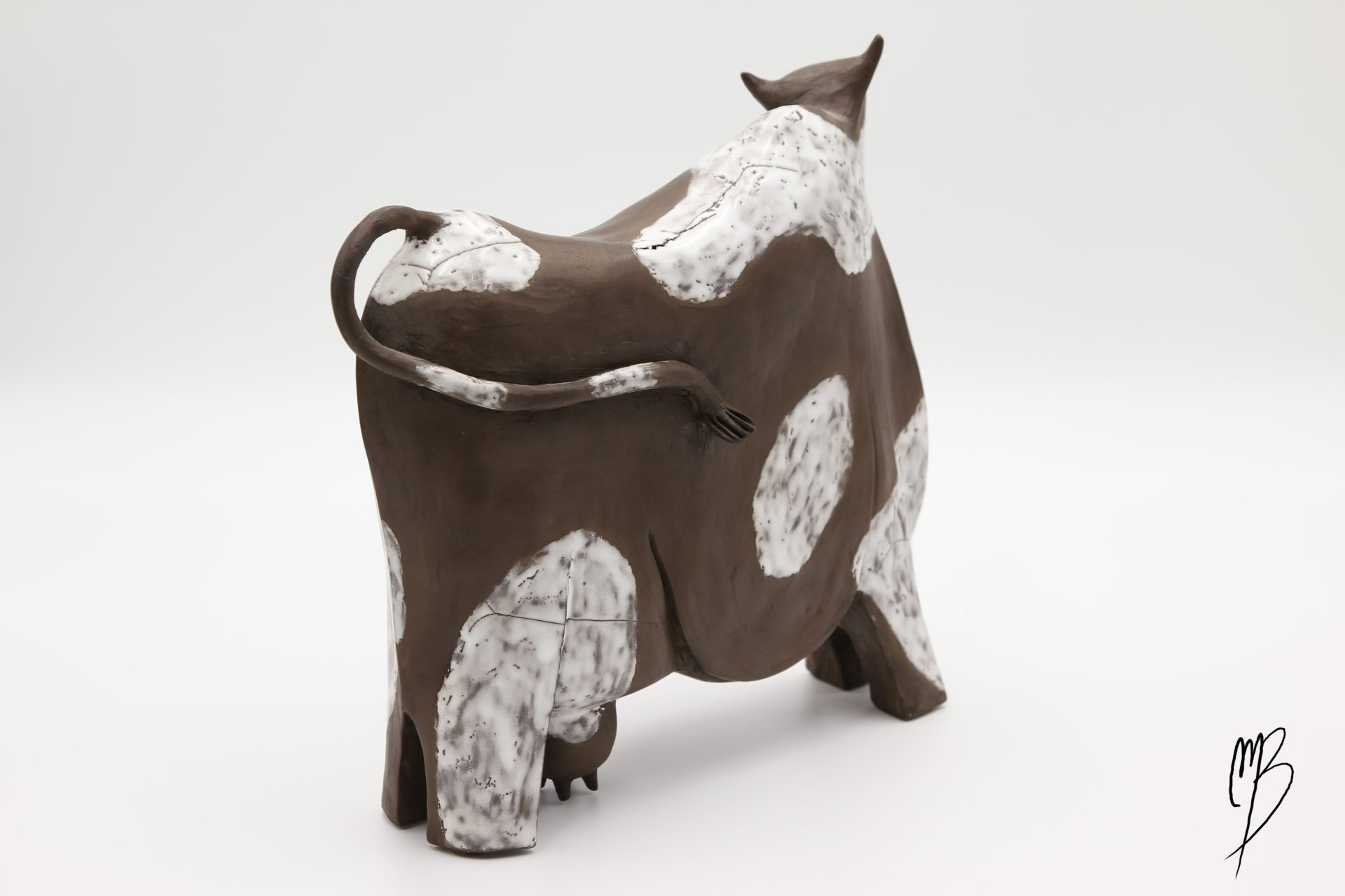 Animaux. Vache stylisée marron en terre cuite avec des tâches blanches émaillées. Vue de dos.