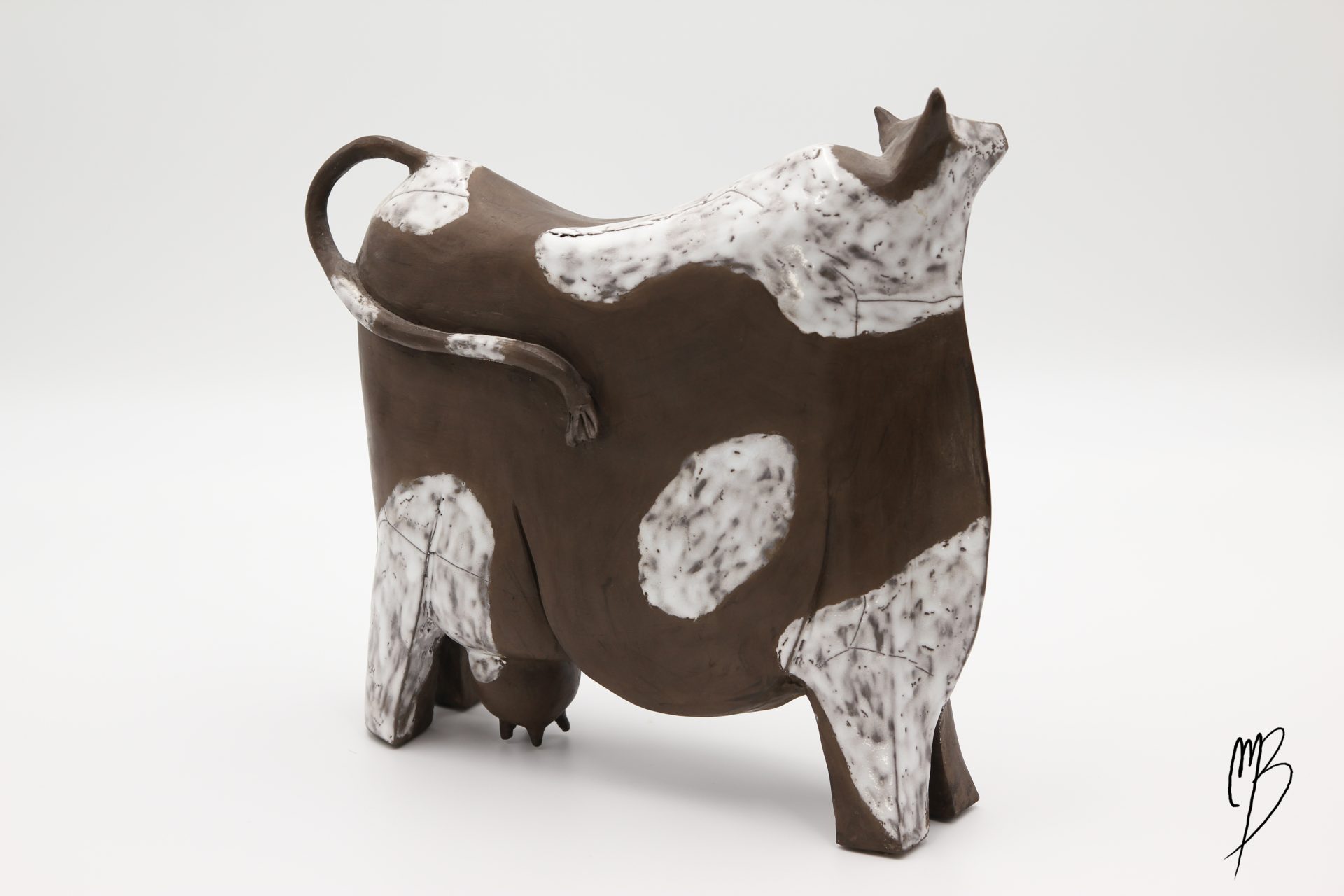 Animaux. Vache stylisée marron en terre cuite avec des tâches blanches émaillées. Vue de côté.