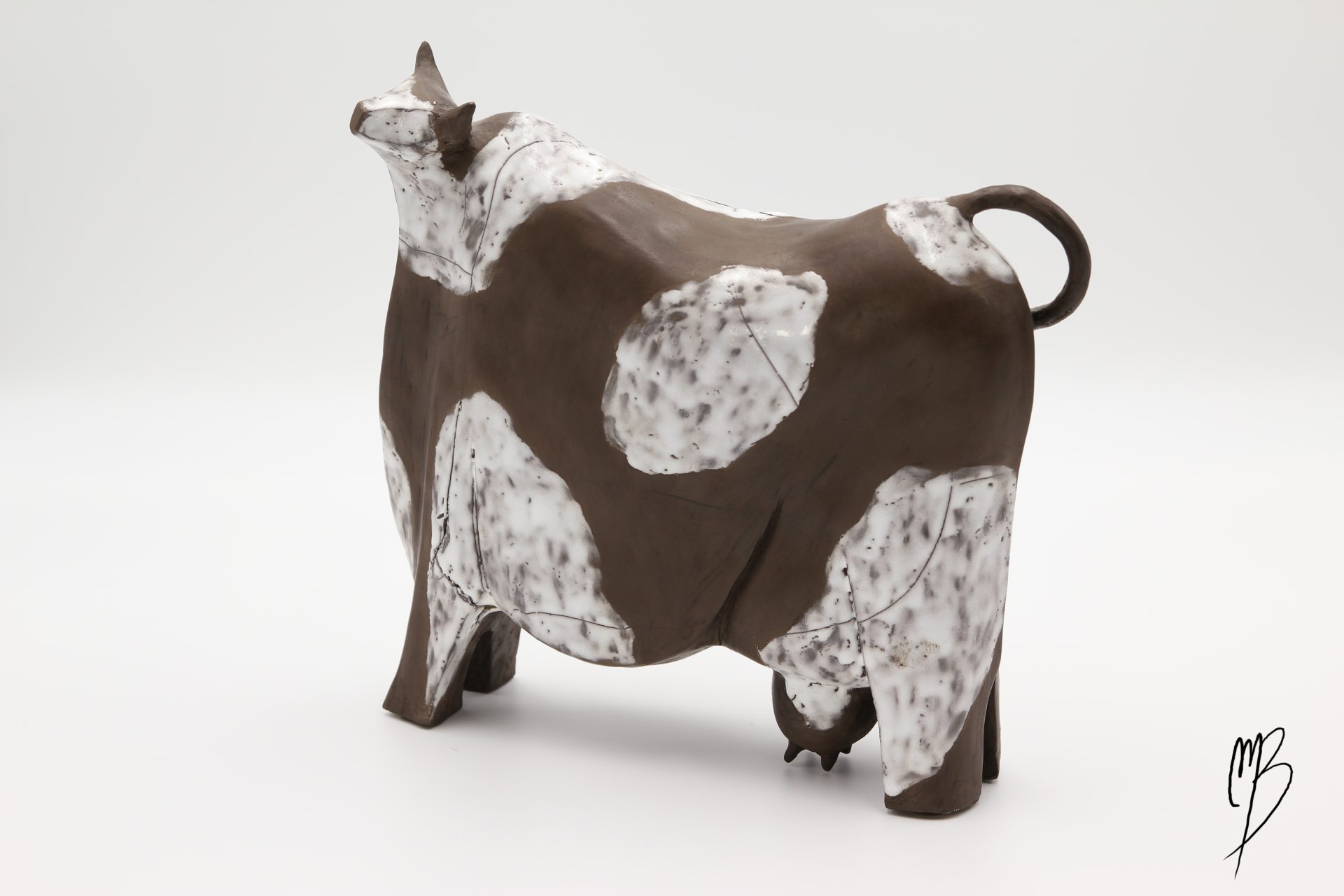 Animaux. Vache stylisée marron en terre cuite avec des tâches blanches émaillées. Vue de côté