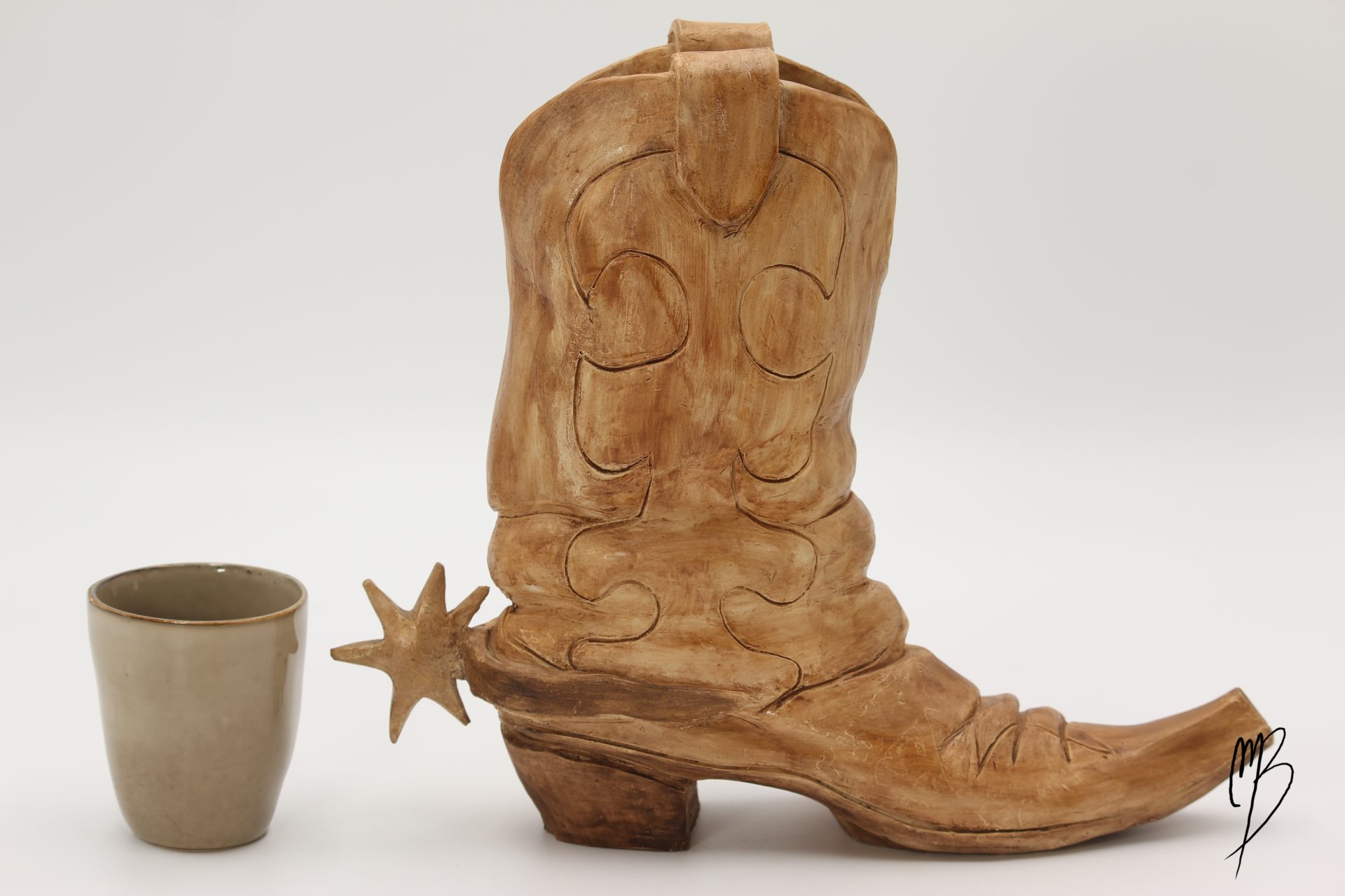 Botte de cowboy Santiag avec son éperon en terre cuite patinée avec une peinture acrylique ocre terre du désert. Vue comparative à une tasse pour la taille.