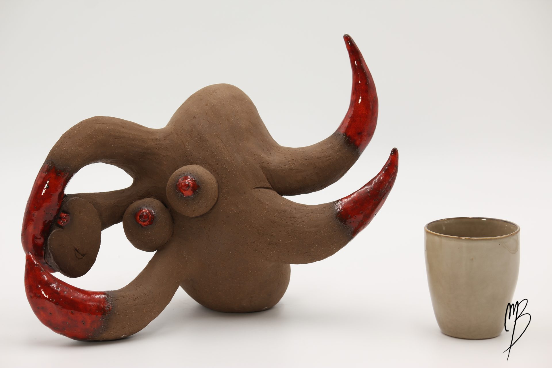 galipette en Terre chamottée cuite avec des éléments patinés de rouges émaillé. Vue comparative à une tasse pour la taille.