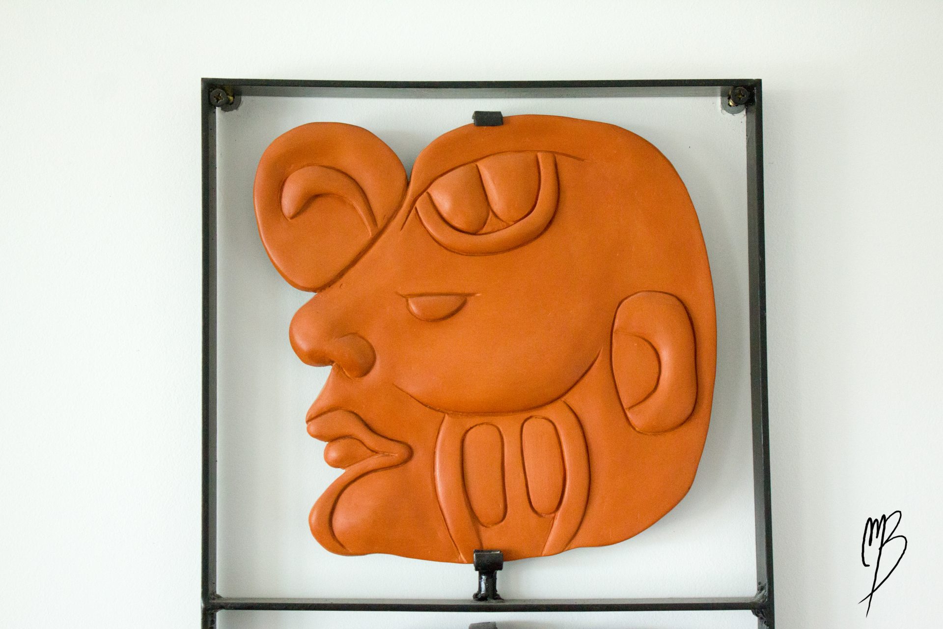 Glyphe composé de trois têtes Maya en terre cuite cirées sur cadre métal, vue partielle d'une tête Maya de profil, élément haut du cadre