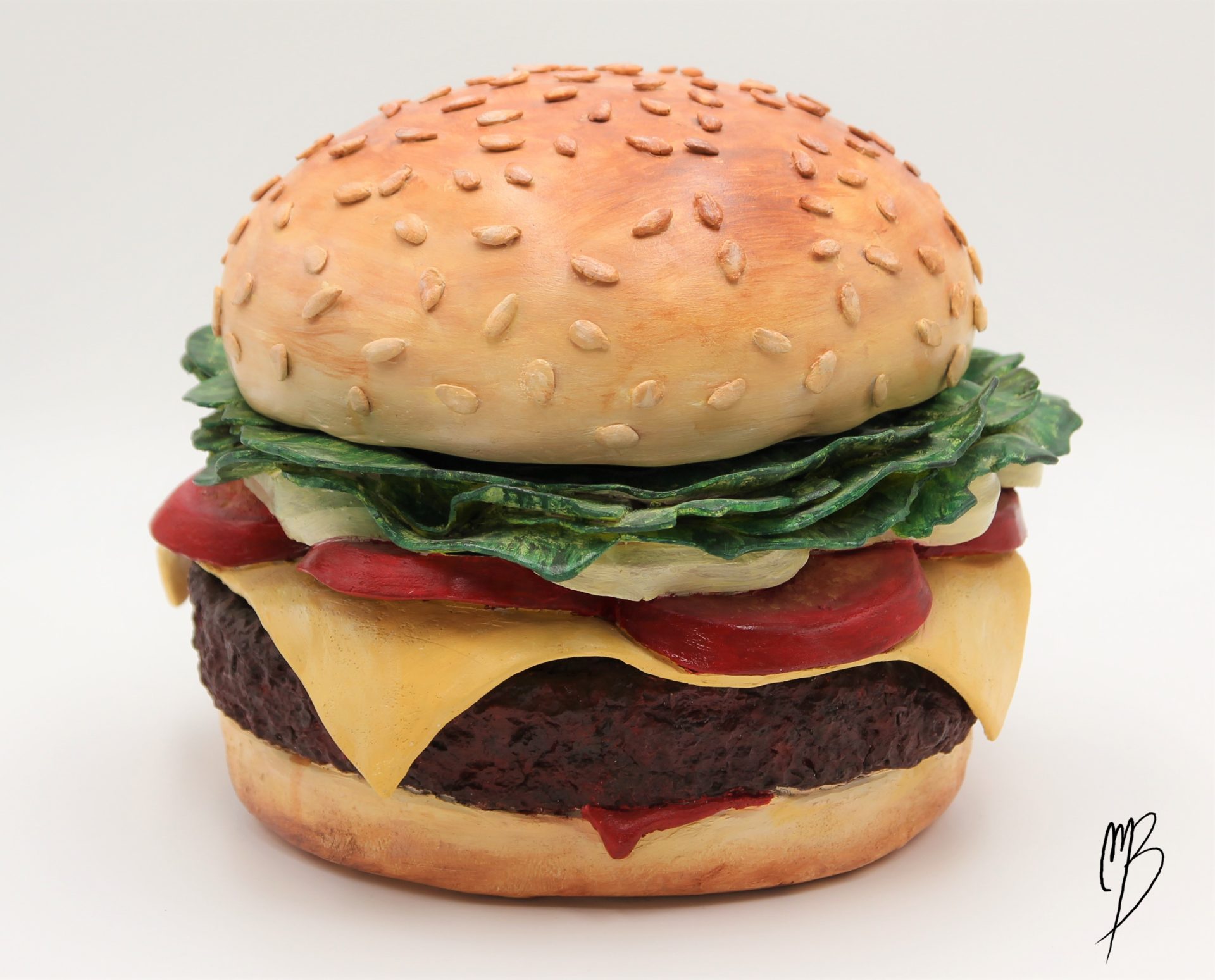 Terre cuite patinée avec des peintures acryliques rouges vertes jaunes marrons. Elle représente un hamburger composée de deux tranches de pain, un steak haché, des tomates en tranche, du fromage fondu et de la salade. Vue générale de face