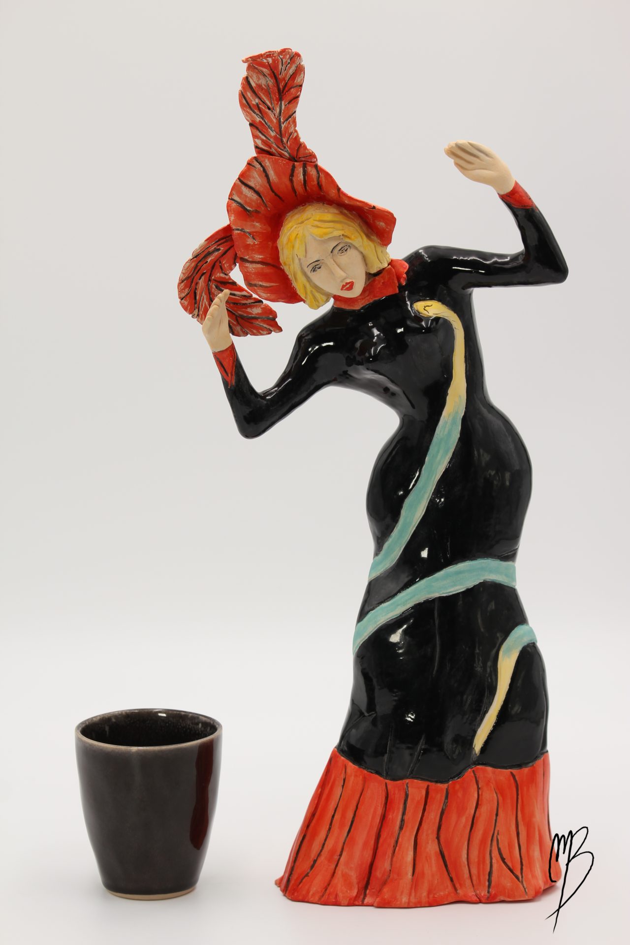 Jane Avril en terre cuite recouverte d'e peintures acryliques vernis rouges, noire, vers, jaune, couleur peau. Vue comparative à une tasse pour la taille.