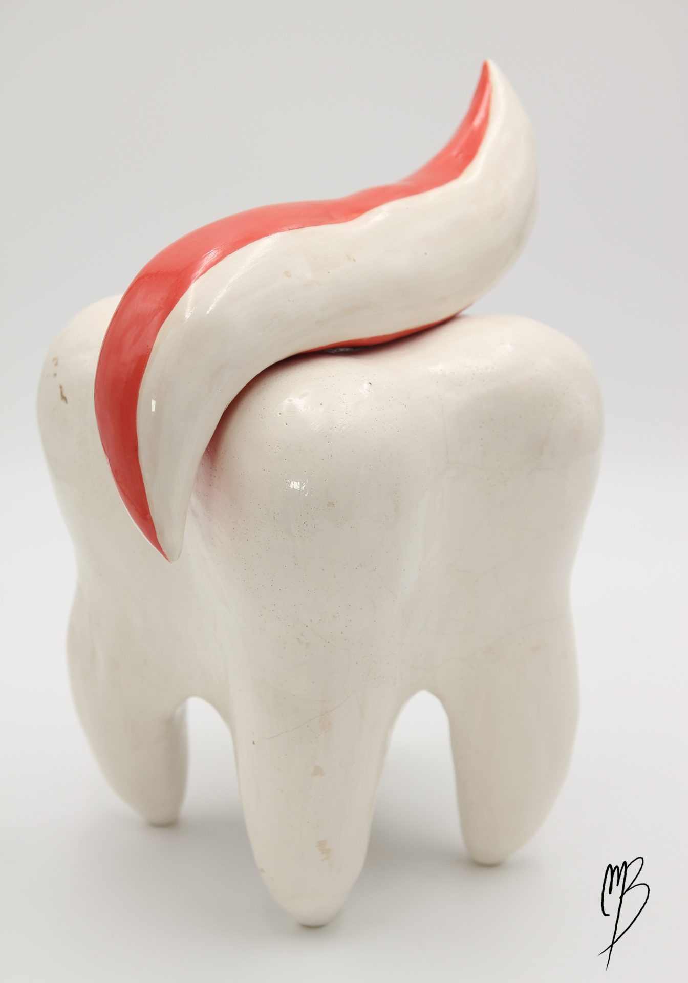 Sculptures. Dent blanche émaillée vernie reposant sur ses racines recouverte de dentifrice rouge et blanc.
