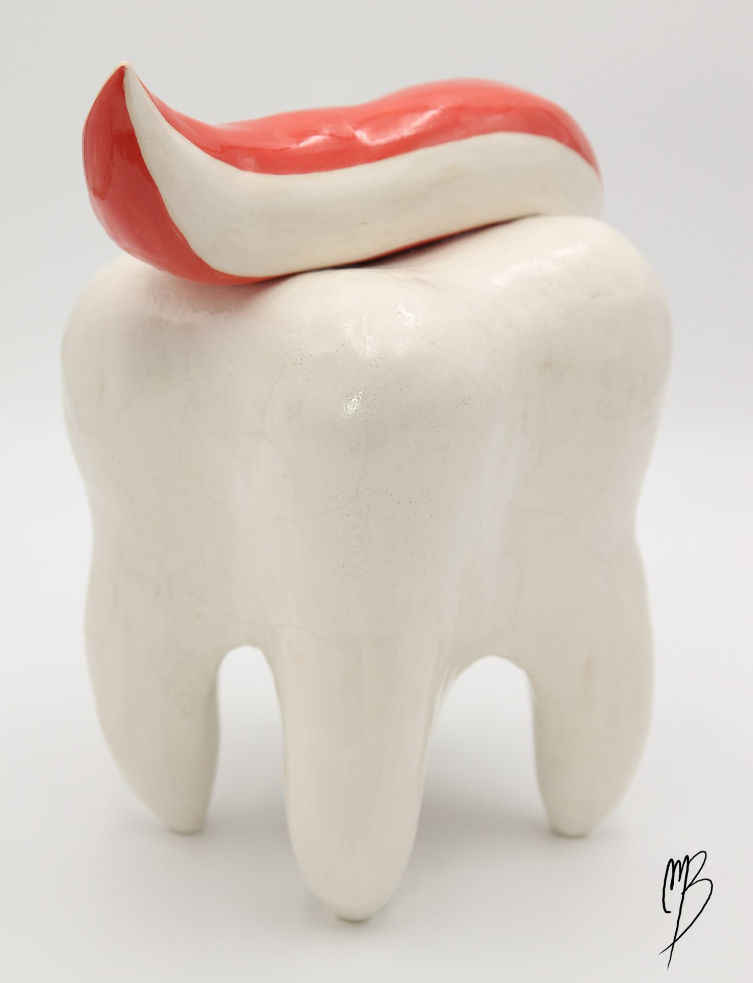 Dent blanche émaillée vernie reposant sur ses racines recouverte de dentifrice rouge et blanc. Vue arrière
