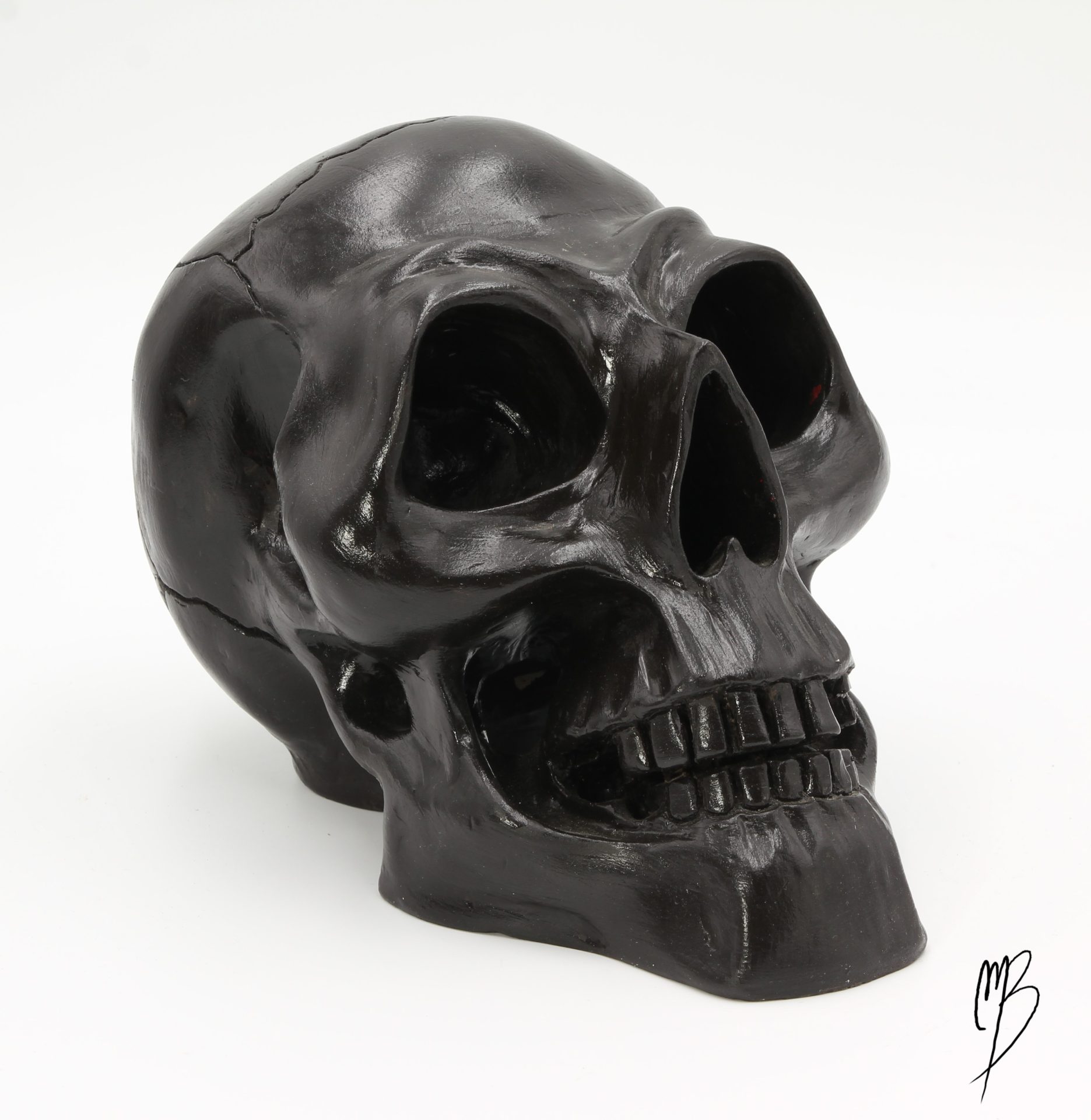 Sculptures. Tête de mort en terre cuite recouverte de peinture acrylique noire et vernie. Vue de face.