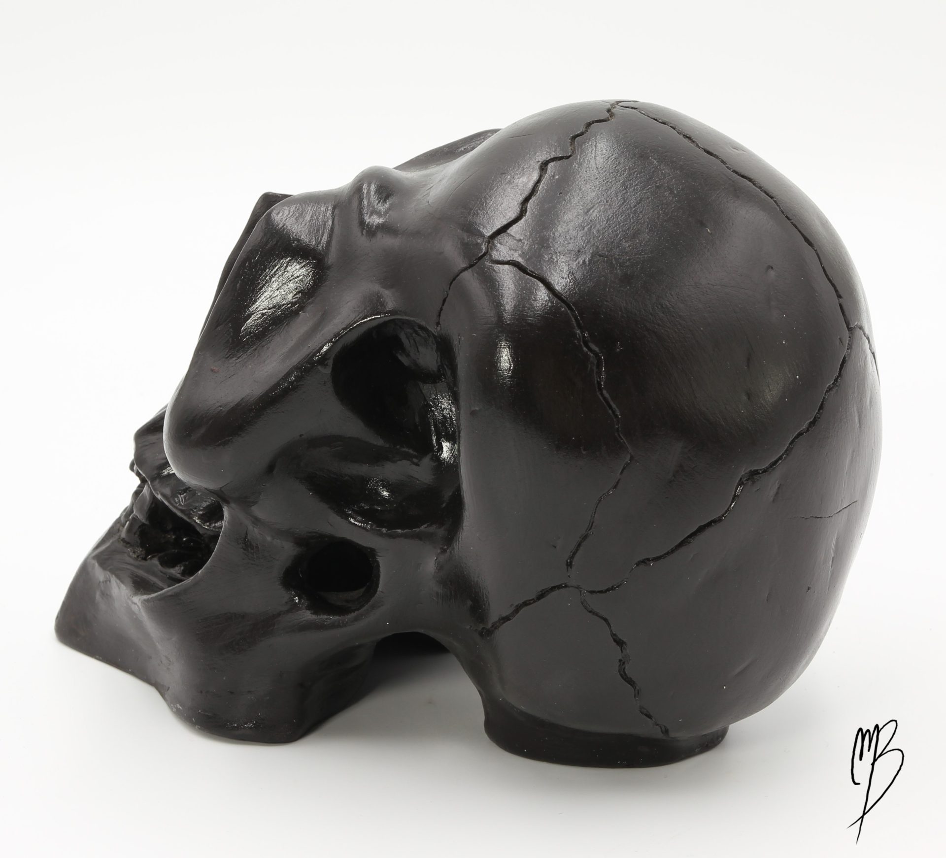 Tête de mort en terre cuite recouverte de peinture acrylique noire et vernie. Vue de côté. Crâne fissuré.