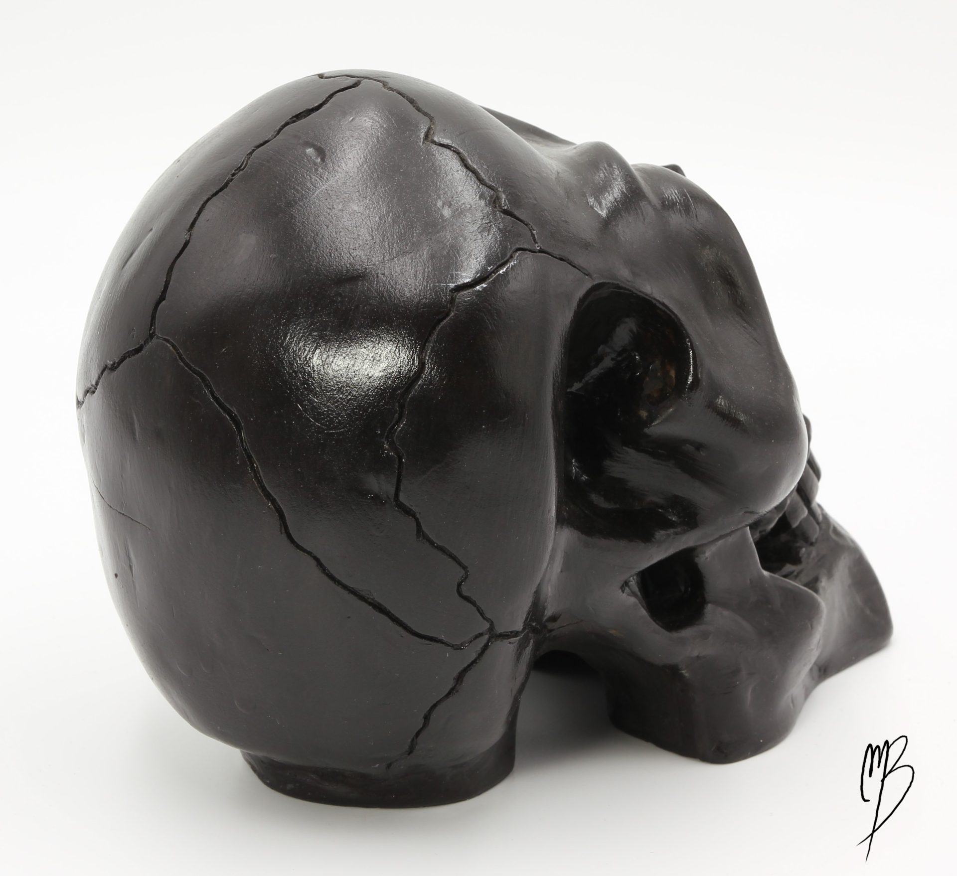Tête de mort en terre cuite recouverte de peinture acrylique noire et vernie. Vue de l'arrière avec le crâne fissuré.