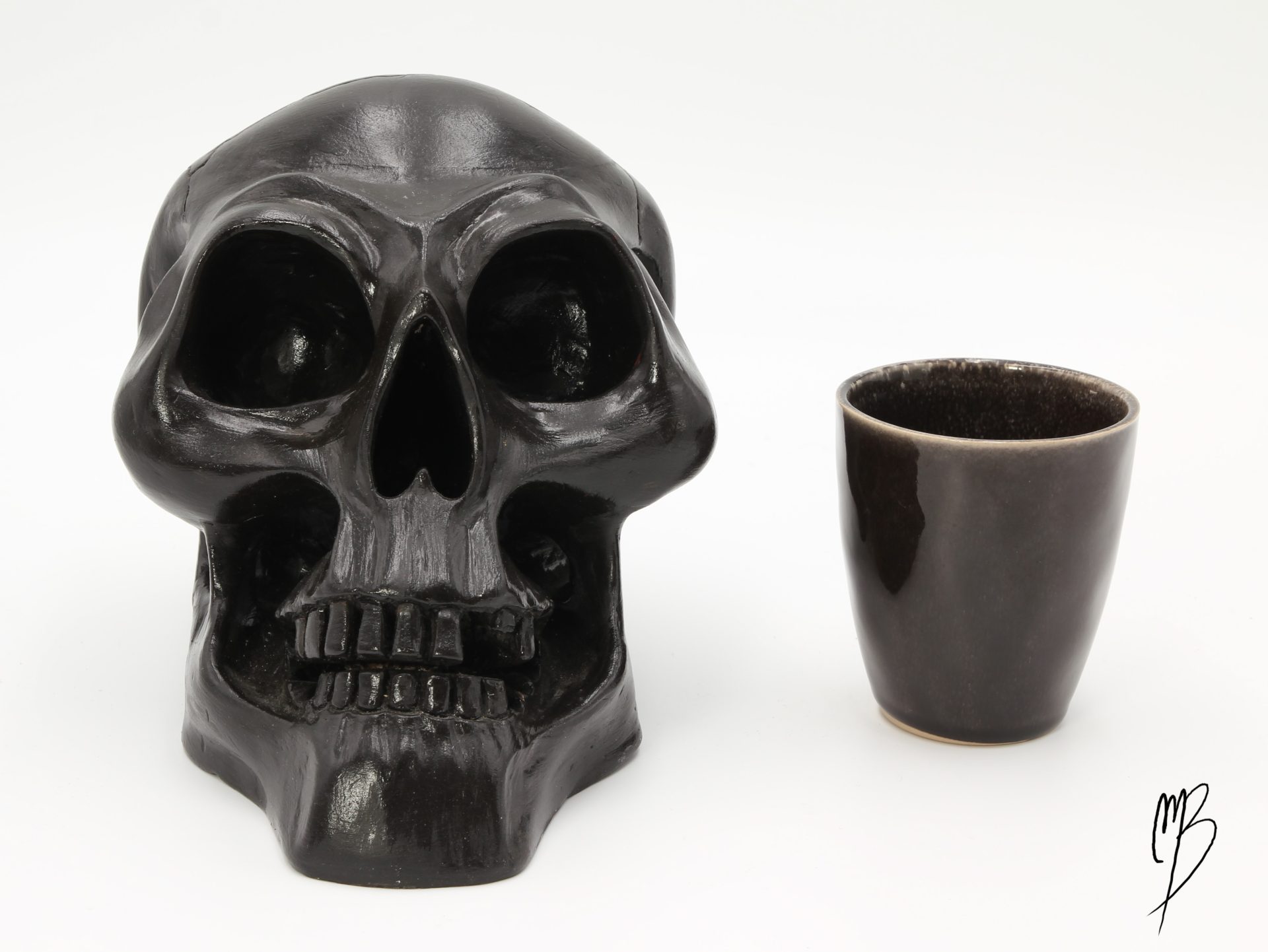 Tête de mort en terre cuite recouverte de peinture acrylique noire et vernie. Vue de face comparative à une tasse pour la taille.