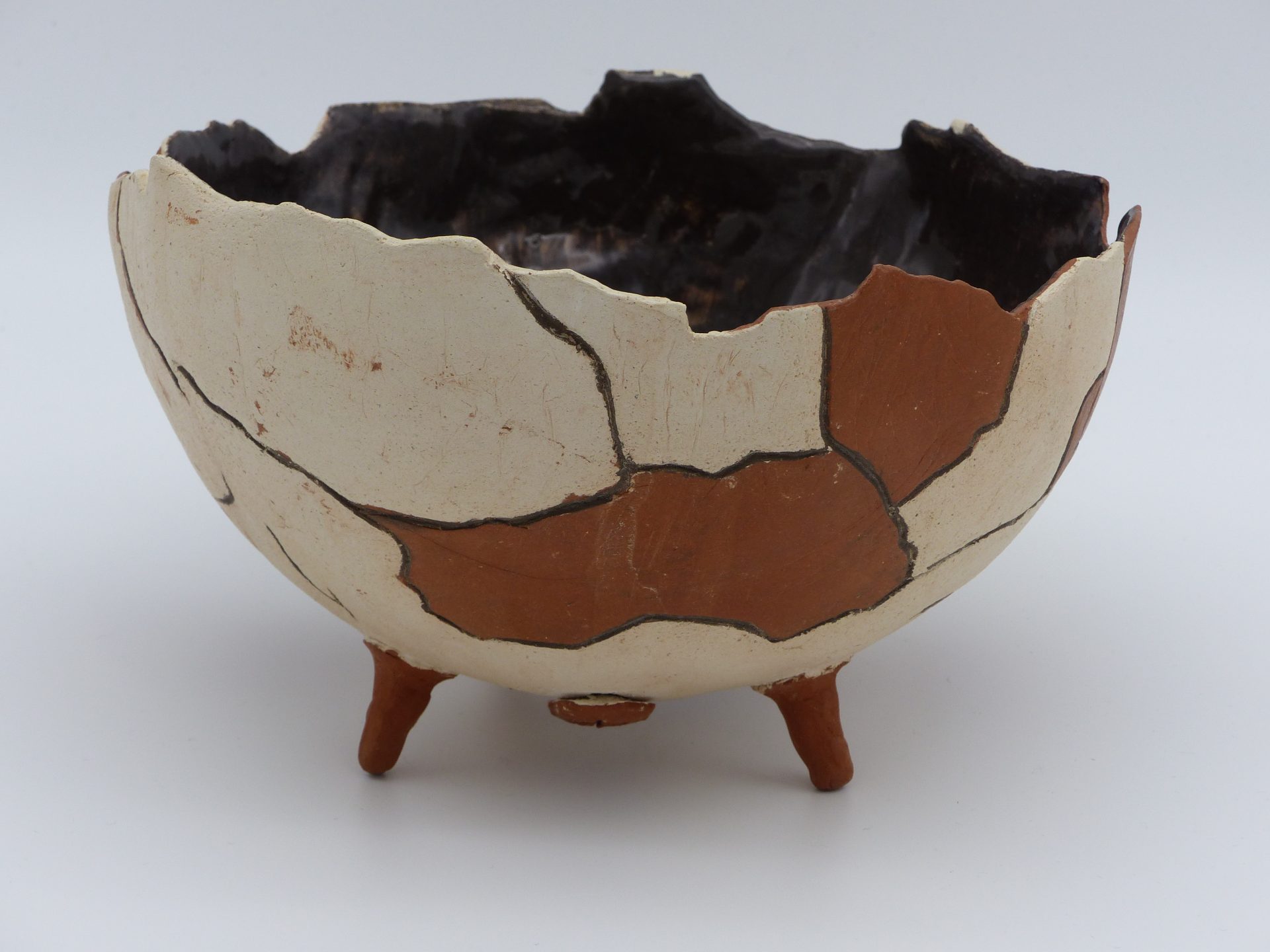 demie coupe façon poterie antique brisée, posée sur trois petits pieds, en terre cuite, avec l'intérieur émaillé noir, et l'extérieur bicolore marron et beige ciré, vue de côté